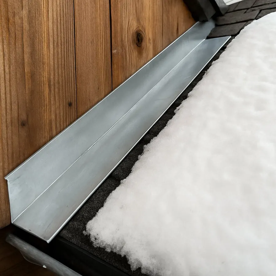 Solin en zinc entre le bardage bois et la neige sur le toit