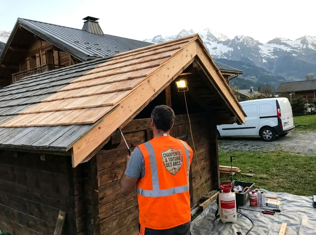 Artisan en gilet orange devant un avant-toit couvert de tavaillons neufs en mélèze